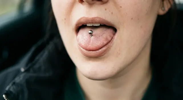 Close-up shot of a person showing a standard vertical tongue piercing with a silver metal barbell stud.